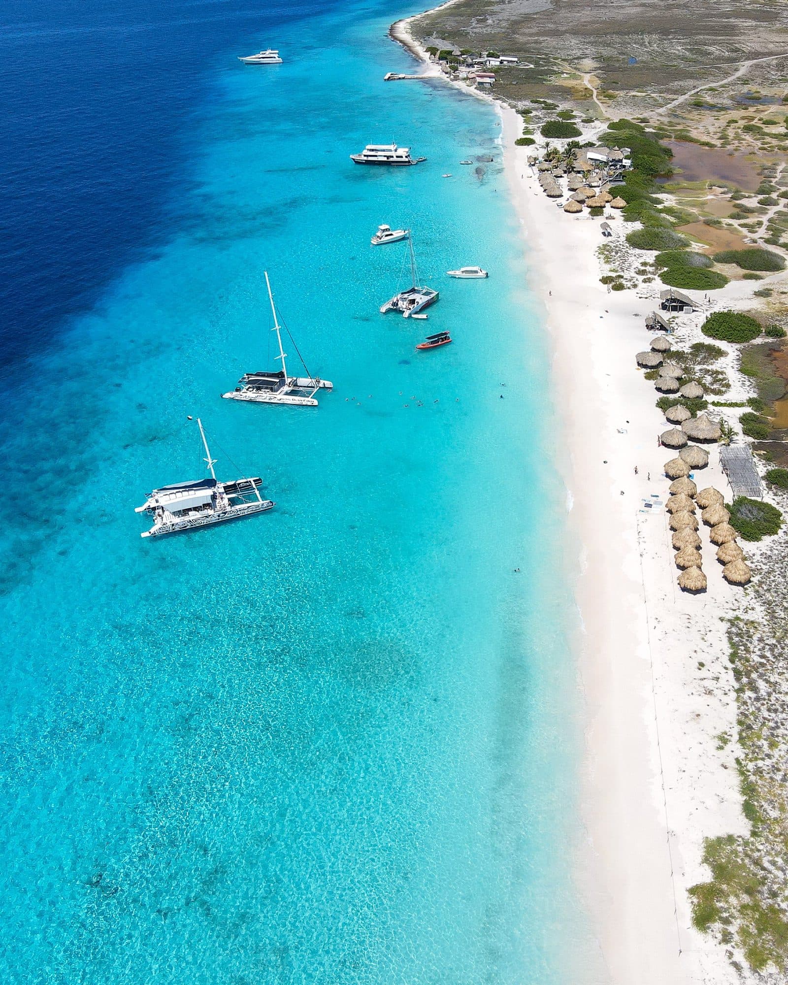 Aerial view of a white-sand beach with boats anchored in turquoise water