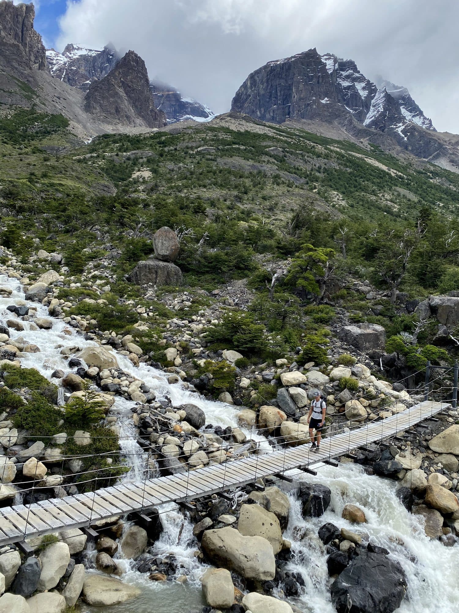 A suspension bridge crossing a rushing stream below the peaks